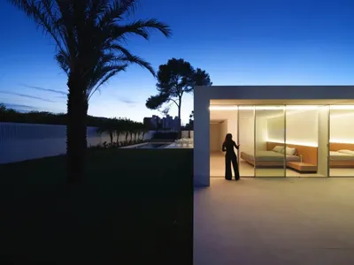A well-lit living room with a couch, chair, and bed, featuring a woman standing near the door, looking outside