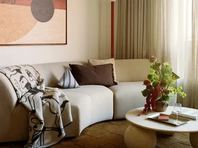 Cozy living room with a white couch, a red lamp, and natural light from the window, decorated with a vase and a potted plant