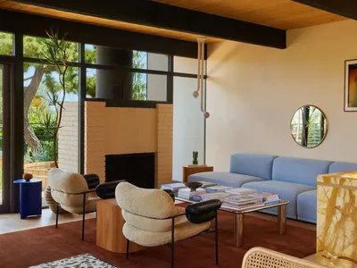 Cozy modern living room with a blue couch, chair, and fireplace, surrounded by books and a vase, with natural light from windows