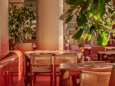 A modern restaurant interior with red tablecloths, red chairs, and large pillars, set in a well-lit dining area