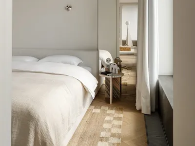 A well-lit bedroom with a bed, a mirror, and a table, surrounded by white walls and wood accents