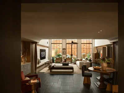 A modern living dining kitchen space with a couch, dining table, chairs, sink, refrigerator, and potted plants, decorated with vases and a bowl, under warm and inviting lighting