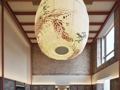A modern restaurant with a bar and dining area, featuring a large open layout, high ceilings, and natural light, with artwork on the walls and various furniture and decorative elements