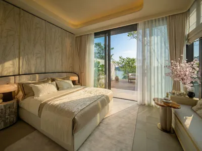 A well-lit bedroom with a bed, chair, and window, featuring white furniture and a clean, organized appearance