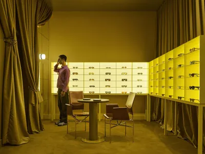 A store with a yellow color scheme, displaying sunglasses in a glass case, with a cozy and inviting atmosphere, and natural light coming in through the windows