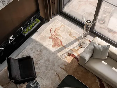 Comfortable and inviting living space with a large rug, couch, chair, and coffee table, surrounded by marble and wood accents, and filled with natural light
