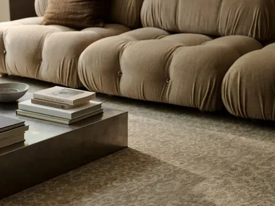 Cozy modern living space with a large couch, coffee table, rug, and books, well-lit by natural light from a window