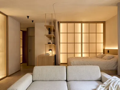 Cozy bedroom with a bed, couch, and bookshelf, set against a white wall and wooden floor, with dim lighting