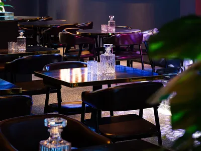 A modern restaurant with a black and white color scheme, featuring a dining area with tables and chairs, a bar, and dim lighting creating a cozy atmosphere