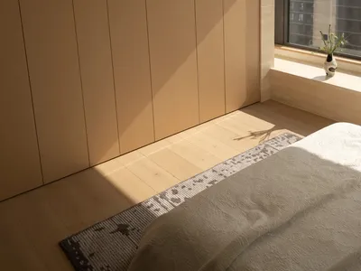 Cozy bedroom with a bed on a wooden floor, a wooden door, and a window in the background, well-lit and inviting