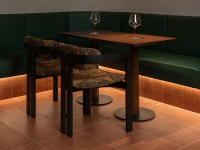 A modern restaurant dining area with a wooden floor, a dining table, chairs, and wine glasses, illuminated by a light source, creating a warm and inviting atmosphere
