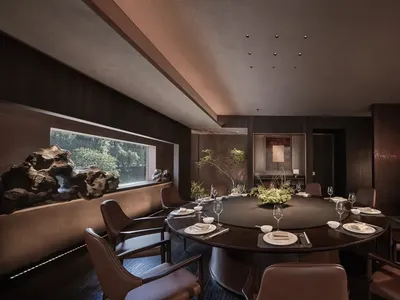 A dimly lit dining room with a round table set for a meal, surrounded by black chairs in a brown room