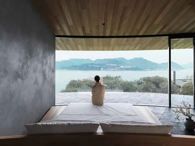 Serene bedroom with a large window offering an ocean view, a wooden headboard, and a white bed sheet in a well-lit space