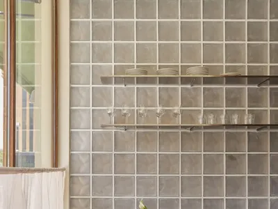 Modern kitchen with a wooden cabinet, tile backsplash, and natural light from a window, featuring wine glasses and a bowl on the countertop