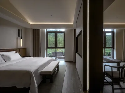 Cozy bedroom with a wooden floor, a bed, and a chair near a window, well-lit and inviting
