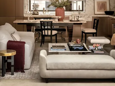 Cozy living room with a couch, chair, and potted plant, adjacent to a dining area with a table and chairs, decorated with books, a vase, and a bowl, featuring a mix of wood and fabric materials and natural lighting