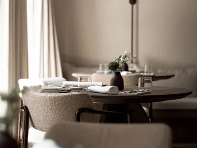 A modern restaurant dining area with white tablecloths, potted plants, and elegant decor, featuring a warm and inviting atmosphere