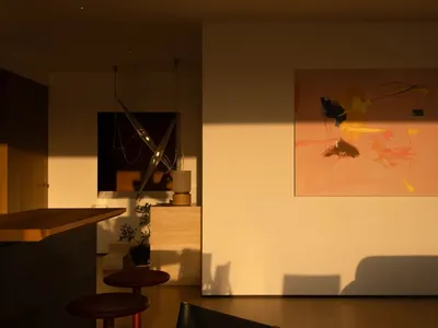 A well-lit living room with a couch, chair, and dining table, featuring a large painting on the wall