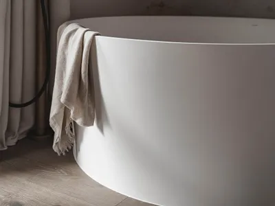 Dimly lit bathroom with a white bathtub under a window, a wool towel hanging on the side, and a cozy atmosphere