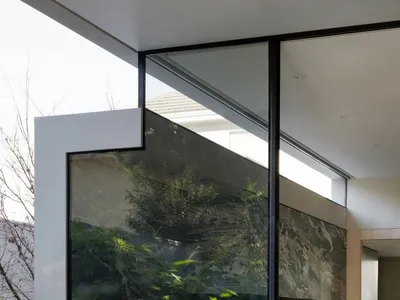 Well-lit living room with a glass wall, large window, dining table, kitchen area, and various furniture pieces