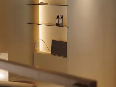 Bathroom with a shelf filled with bottles and a book, featuring a white color scheme and soft warm lighting