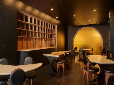 A modern restaurant with a large dining area, bar, and comfortable seating, featuring a variety of tables, chairs, and bottles on display