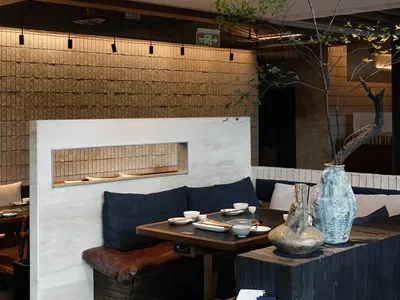 Cozy modern restaurant dining area with a wooden table, chairs, and a potted plant, set with bowls and cups, in a warm and inviting atmosphere