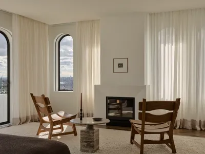 Cozy living room with a fireplace, wooden furniture, and a rug, surrounded by natural light from the windows