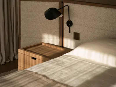 A well-lit bedroom with a bed, nightstand, and lamp, featuring wood and fabric materials in a calm and relaxing environment
