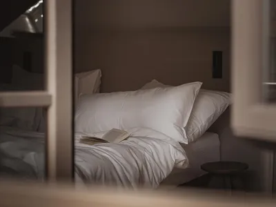 舒適的臥室,床、椅和書,從窗戶自然光照,木材和布料可見