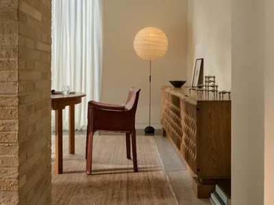 Cozy living room with a brick wall, hardwood floor, a red chair, a table, and a lamp, well-lit and inviting