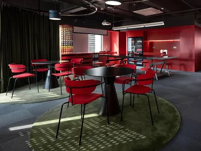 A modern dining space with a red and black color scheme, featuring a dining table and chairs, a kitchen area with a refrigerator and sink, and dim lighting creating a warm and intimate ambiance