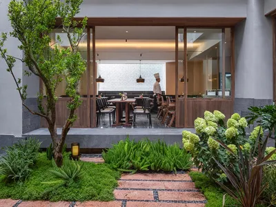 A modern restaurant with a dining area featuring a wooden table and chairs, and a kitchen with metal appliances and a neutral color scheme