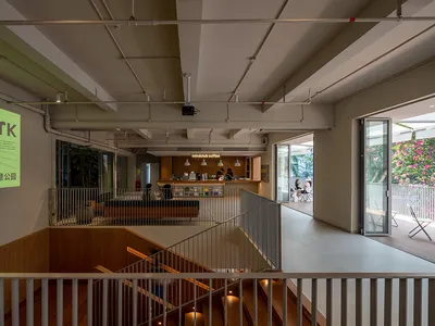 A large, open space with a staircase, balcony, and comfortable seating areas, featuring wood and metal materials and well-distributed lighting