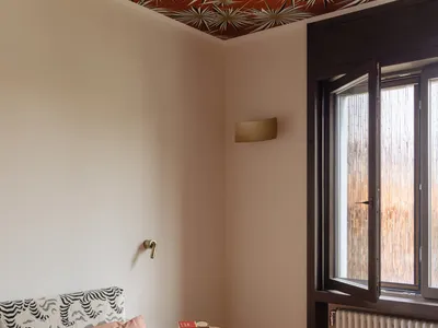 Cozy bedroom with a pink-covered bed, a small table, and a window allowing natural light, with a radiator for warmth