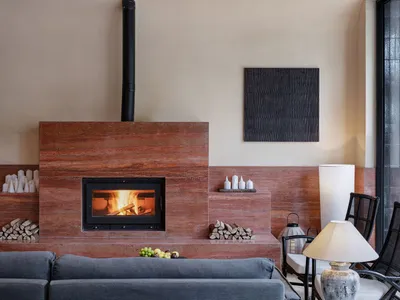 Cozy living room with a fireplace, couch, chair, and dining table, decorated with books, vases, and bottles, with dim warm lighting