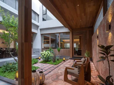 Open living room with a wooden floor, natural light, and modern furniture, including a couch, chair, and dining table, with a potted plant adding greenery
