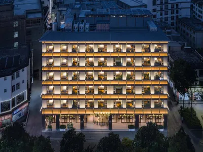 一座高聳飯店建築，擁有黃色木質立面，背後是城市天際線，其他建築與傍晚燈光