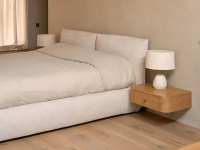 Cozy bedroom with a white bed, tan comforter, wooden nightstand, and natural light from an open window