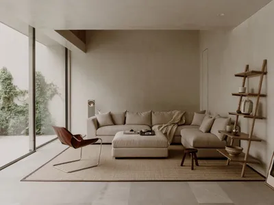 A modern living room with a large couch, a chair, and a coffee table, featuring a vase, a bowl, a book, and a remote control, with a neutral color palette and minimal decorations