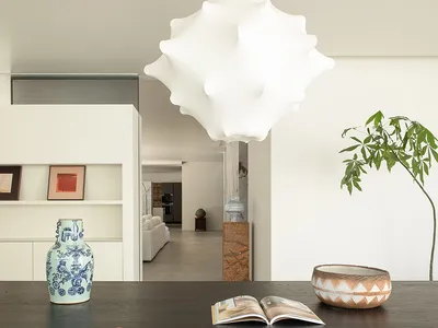 A modern living room with a dining table, chairs, and a vase, surrounded by a large white wall, a potted plant, a bowl, and a book, creating a comfortable and inviting atmosphere