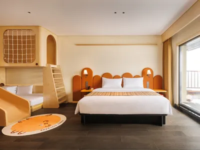 Cozy bedroom with a bed, chair, and desk, surrounded by white walls and natural light