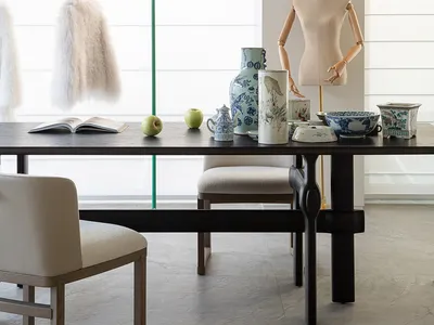 A modern dining room with a table set for a meal, surrounded by black furniture and natural light from a large window