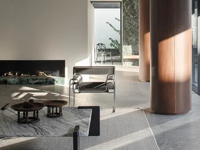 Cozy living room with a fireplace, couch, chair, and dining table, decorated with vases, bowls, and potted plants, and featuring wood, stone, and glass materials in a well-lit space with natural light