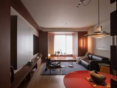 Cozy modern living room with a red table, a couch, a chair, and a TV, decorated with a vase, a bowl, and a book, with natural light and a warm atmosphere