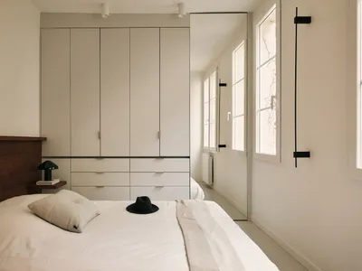 A minimalist bedroom with a white bed, dresser, and natural light from an open window