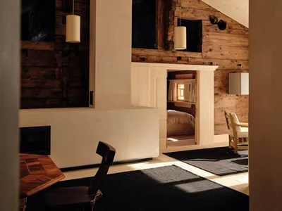 A well-lit living room with a wooden floor, a fireplace, a dining table, a couch, a chair, and a bed, giving a cozy and rustic feel