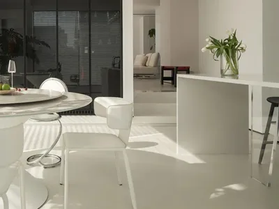 A bright and airy living space with a large window, white furniture, and a dining table, chairs, and couch, creating a comfortable and inviting atmosphere