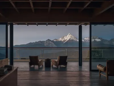 Cozy living room with two couches, a dining table, and a potted plant, featuring a large window with a stunning mountain view