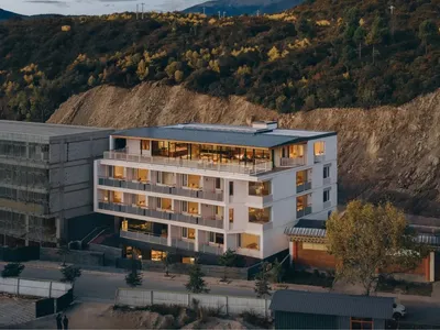 A modern hotel building with a concrete exterior, surrounded by trees and natural scenery, with soft and diffused lighting